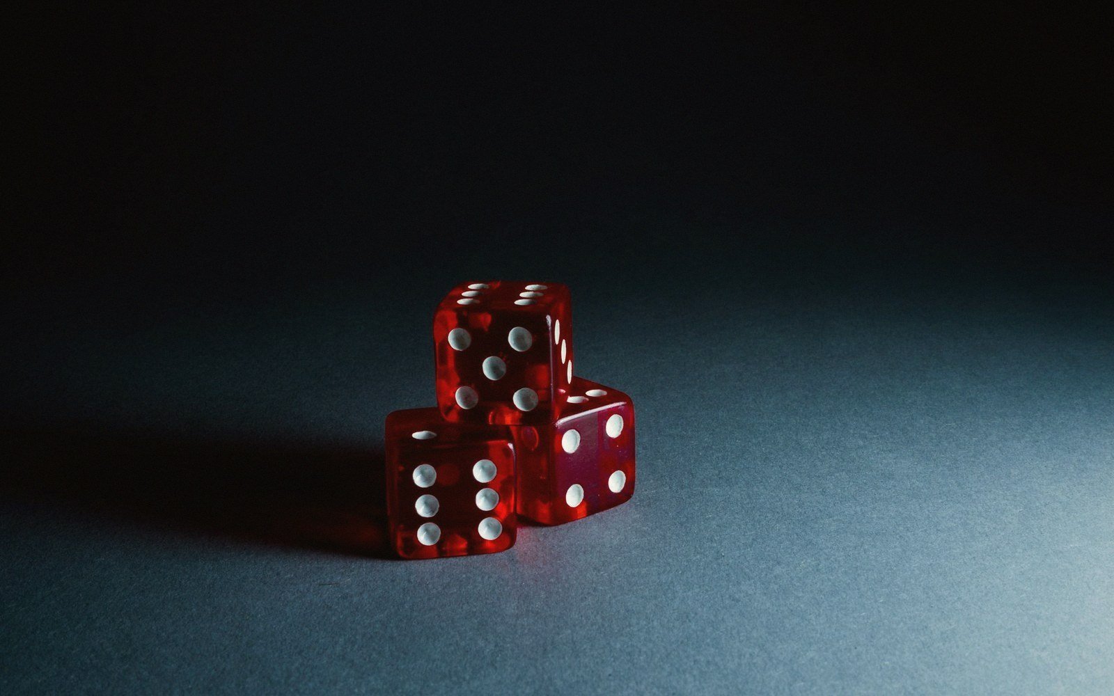 Three red translucent dice stacked together, casting shadows on a gray surface