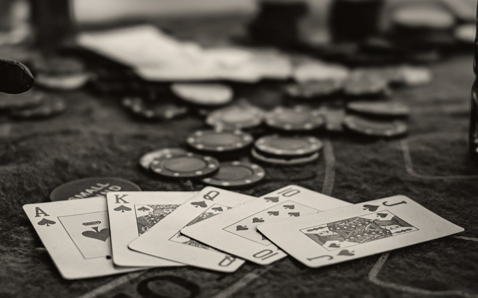Spade cards forming a royal flush lie fanned on a table beside poker chips