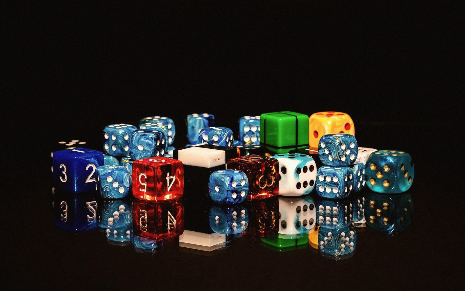 Colorful six-sided dice in various sizes scattered on a reflective black surface