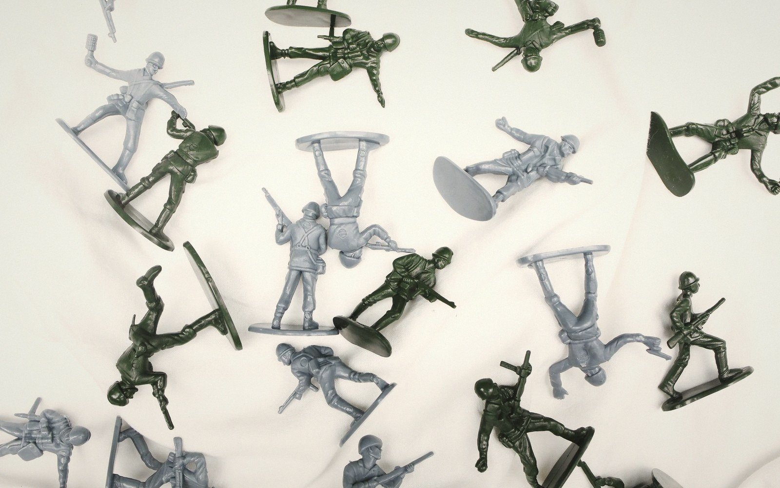 Green and gray plastic toy soldiers scattered face-up and upside down on fabric