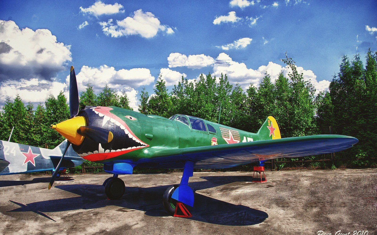 A propeller fighter plane with a painted shark-mouth nose sits parked outdoors