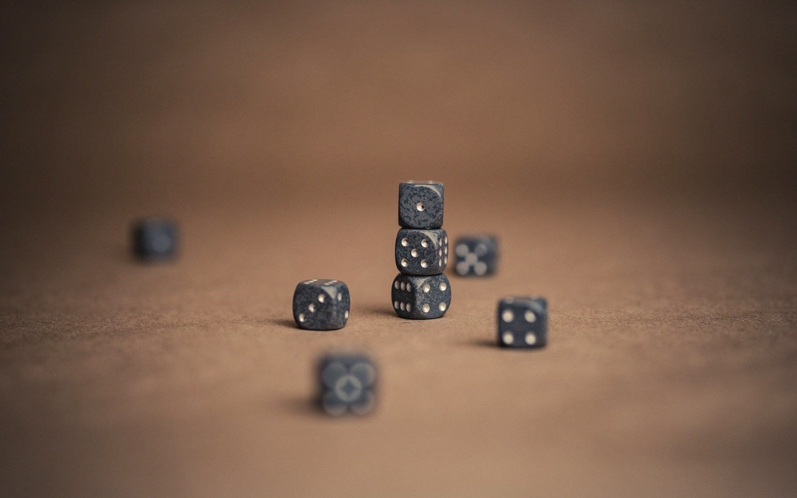 Small black dice with white pips stacked and scattered on a brown surface